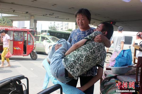 來到街頭“賣唱”點，呂愛梅熟練地把兒子把下三輪車，布置場地。 馬義恒 攝